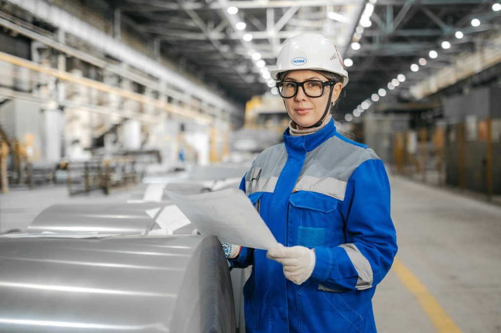 A female engineer wearing safety gear inspects machinery in an industrial factory setting.